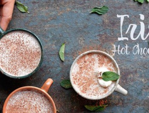 Three cups of hot chocolate set atop a table with green leaves scattered between the mugs.