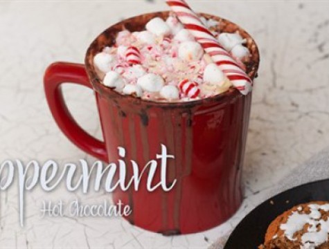 Red cup of peppermint hot chocolate topped with mini marshmallows and candy canes.
