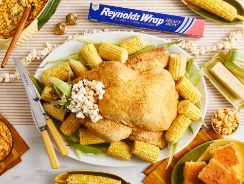 A cooked turkey on a plate, surrounded by corn with popcorn on top. A box of Reynolds Wrap heavy duty foil is nearby.