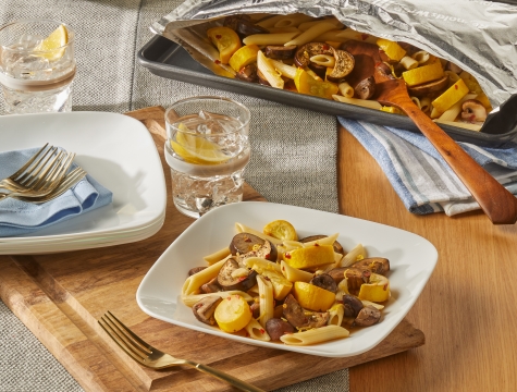 Lemony pasta with eggplant, mushroom and yellow squash served on a white plate sitting alongside an open aluminum foil grill page with additional servings inside