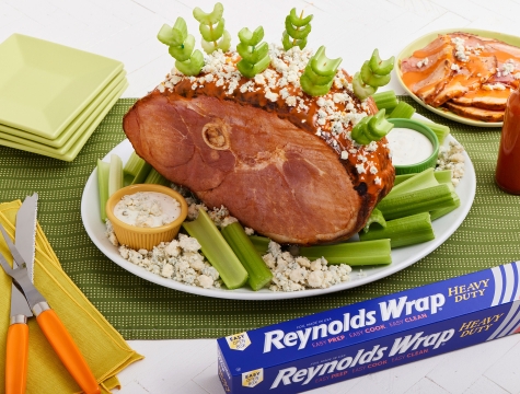 Cooked Ham with Buffalo Glaze and topped with celery and blue cheese crumbles sitting on a platter alongside a box of Reynolds Wrap Heavy Duty Foil