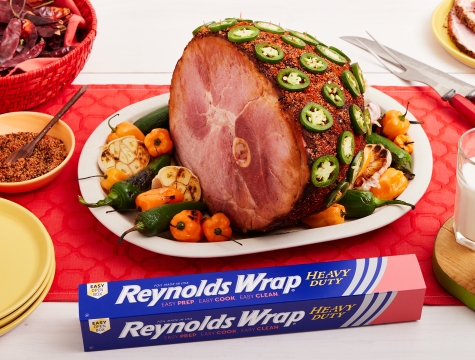 Cooked Ham with Habanero Chipotle Glaze and topped with sliced peppers sitting on a platter alongside a box of Reynolds Wrap Heavy Duty Foil
