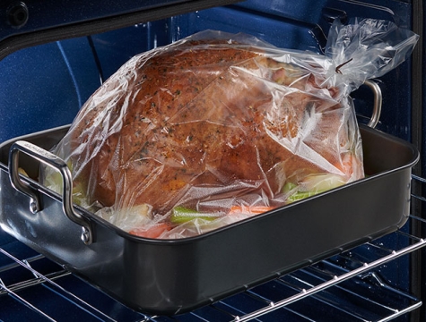 Cooked turkey in an oven bag sitting in a roasting pan on an oven rack
