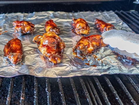 Person using tongs to remove a chicken wing from aluminum foil sitting on top of a grill grate