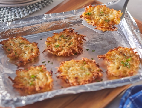 Person using a spatula to remove a potato pancake from an aluminum foil lined baking sheet