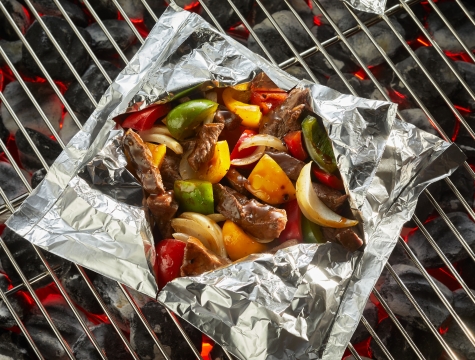 aluminum foil pack filled with beef, bell peppers and onions sitting on a grill grate 