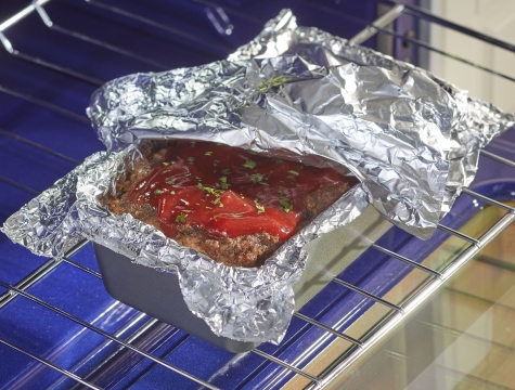 Meatloaf partially covered by aluminum foil sitting on an oven rack