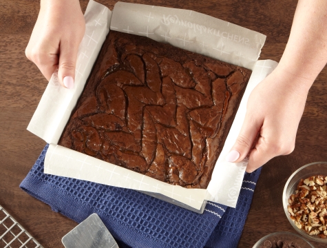 Person removing brownies from a square baking pan with a parchment paper sling