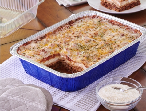 Lasagna is a disposable aluminum pan with a slice removed and sitting on a plate at a kitchen table