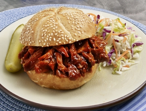 Brisket barbecue sandwich on a sesame seed bun alongside coleslaw and a pickle