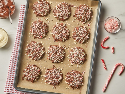 Cookies topped with a white chocolate drizzle and crushed peppermint on a baking sheet lined with unbleached parchment paper