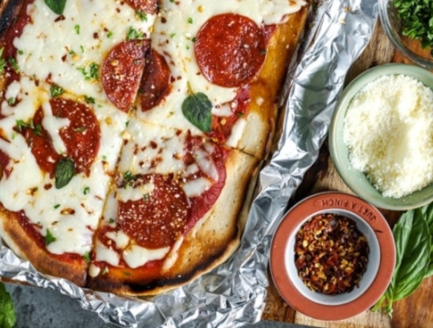 pepperoni pizza sitting on a sheet of aluminum foil alongside additional pizza toppings and seasonings