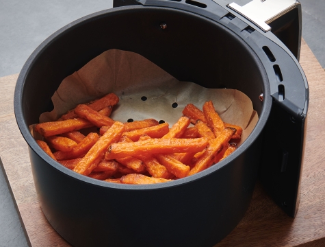 Sweet potato fries sitting in a round air fryer basked lined with a parchment liner