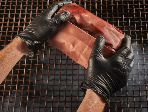 Person placing a piece of meat wrapped in butcher paper on a smoker