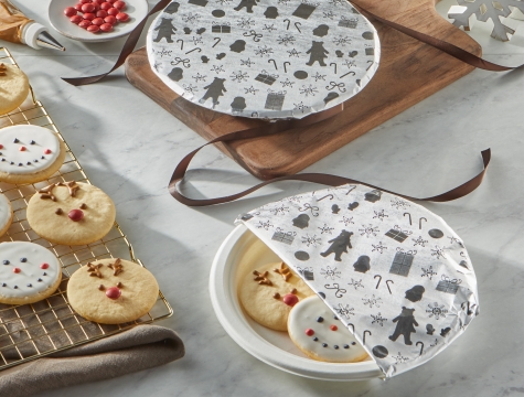 Snowman and reindeer decorated sugar cookies on a plate partially covered with foil