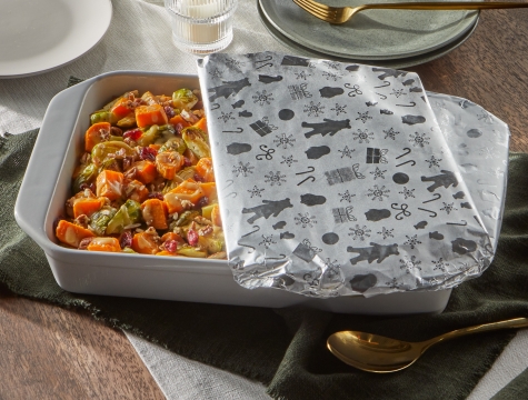 casserole pan filled with roasted sweet potatoes and brussels sprouts sitting on a dining room table partially covered with foil