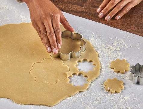 person pressing a cookie cutter down on rolled dough sitting on a piece of countertop prep paper