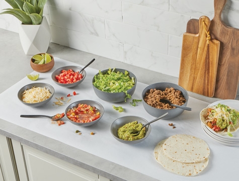 taco ingredients sitting in bowls on a sheet of countertop prep paper on a kitchen counter