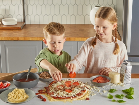two kids making a homemade pizza using Reynolds Kitchens countertop prep paper to protect the kitchen island