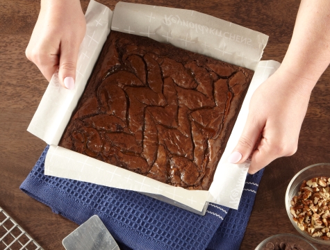 caramel brownies in a square baking pan lined with a parchment sling