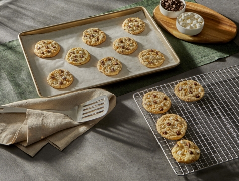 smores cookies on a parchment lined baking sheet alongside a wire cooling rack, spatula and kitchen towel