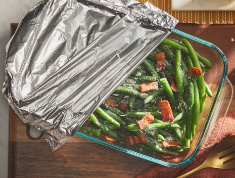 casserole dish filled with green beans partially covered with foil
