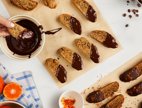 biscotti dipped in chocolate sitting on sheets of unbleached parchment paper