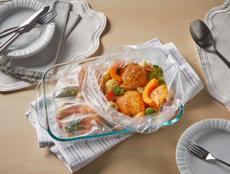 cooked chicken thighs and vegetables in a Reynolds Kitchens Oven Bag sitting in a casserole dish on a set table