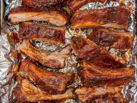 ribs sitting on a sheet of foil alongside a small bowl of BBQ sauce