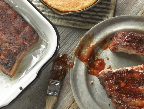rack of ribs in an oven bag alongside a platter and cornbread skillet