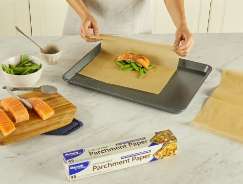 Person folding salmon and snap peas into a parchment packet