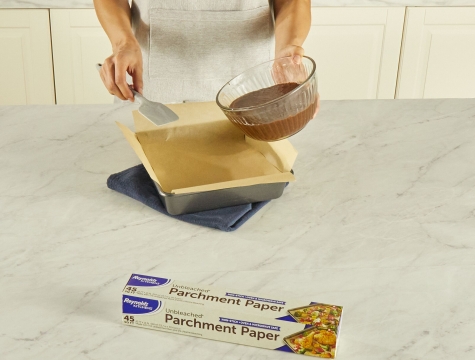 person pouring brownie batter into a pan lined with a parchment paper sling