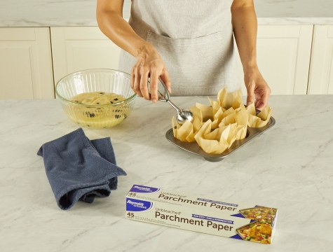 person filling parchment paper tulip muffin liners with muffin batter