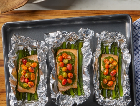 Aluminum foil packets on a baking sheet topped with asparagus and salmon filets