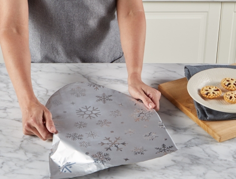 person wrapping a dish with Reynolds Wrap Fun Foil with Snowflakes Pattern