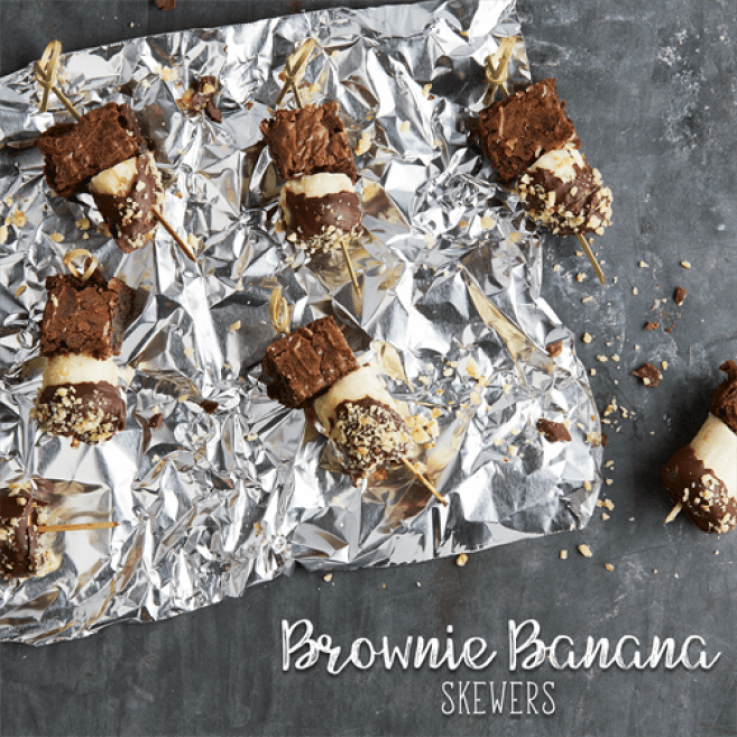 Skewers threaded with brownie bites and chocolate dipped banana topped with crushed nuts set atop Reynold's foil. 