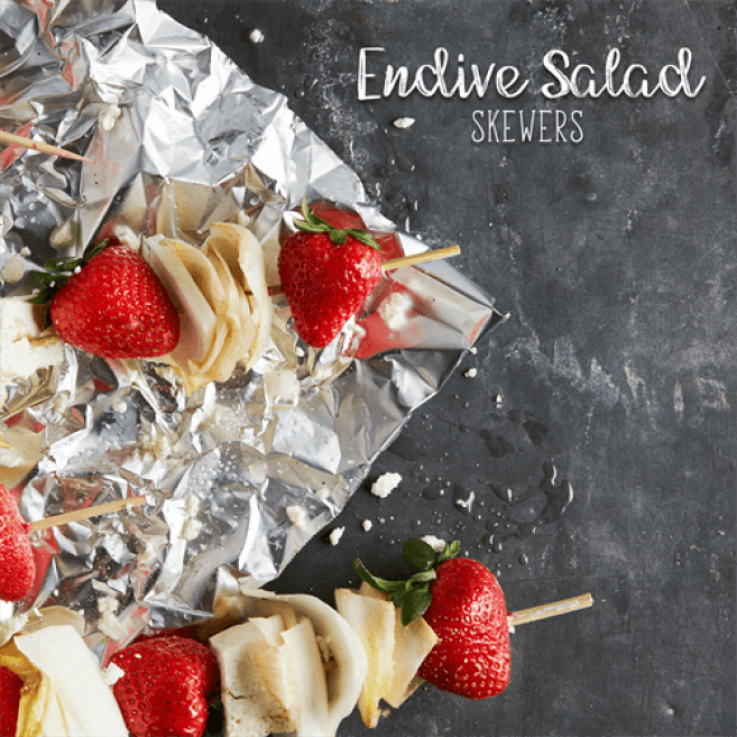 Skewers threaded with strawberries, feta cheese and endive set on top of foil.