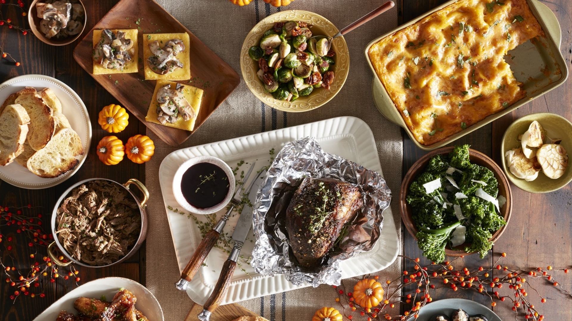 Fall table setting showing foil wrapped pork tenderloin, roasted broccolini and other fall foods