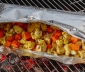 Roasted cauliflower and carrots in an open aluminum foil grill bag sitting on top of a hot grill