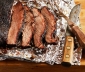 Sliced Brisket on Foil Next to Carving Set