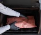 A person adding meat wrapper on pink paper to the grill