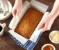 A person pulling baked banana bead out of a loaf pan using a parchment sling