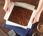 A person pulling baked brownies out of a square pan using a parchment sling