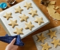 A person holding a parchment lined cookie sheet with star shaped sugar cookies