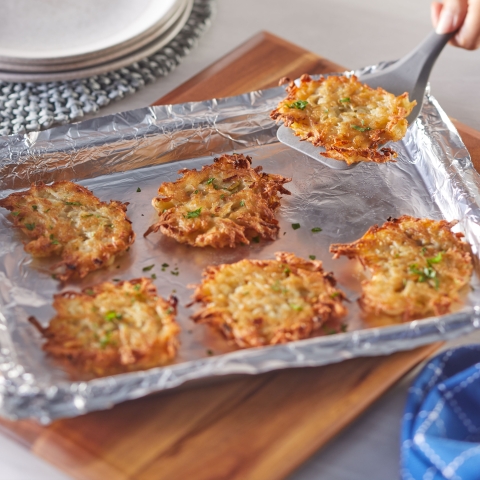 Person using a spatula to remove a potato pancake from an aluminum foil lined baking sheet