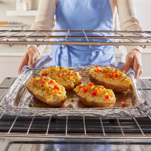 Woman removing twice baked potatoes sitting on an aluminum foil lined baking pan from the ovenrom the oven 