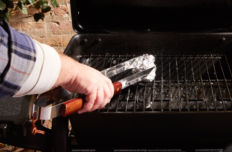 Person using tongs and an aluminum foil ball to clean grill grates