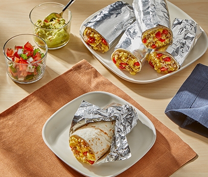 Breakfast burritos wrapped in foil stacked on a plate