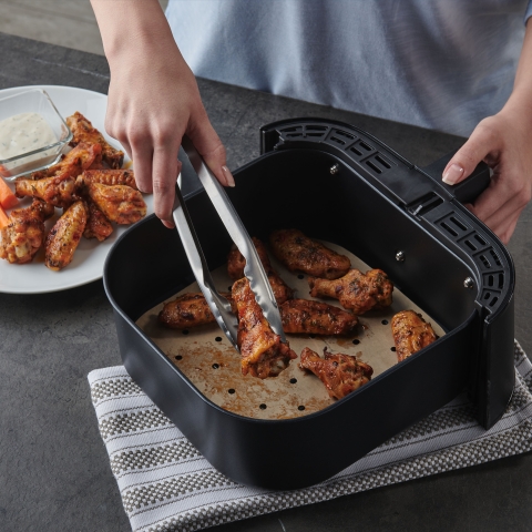 person removing chicken wings from an air fryer basket lined with a Reynolds Kitchens Air Fryer Liner