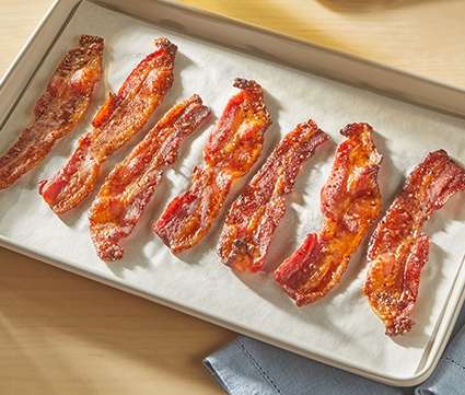 maple glazed bacon sitting on a baking sheet lined with parchment paper